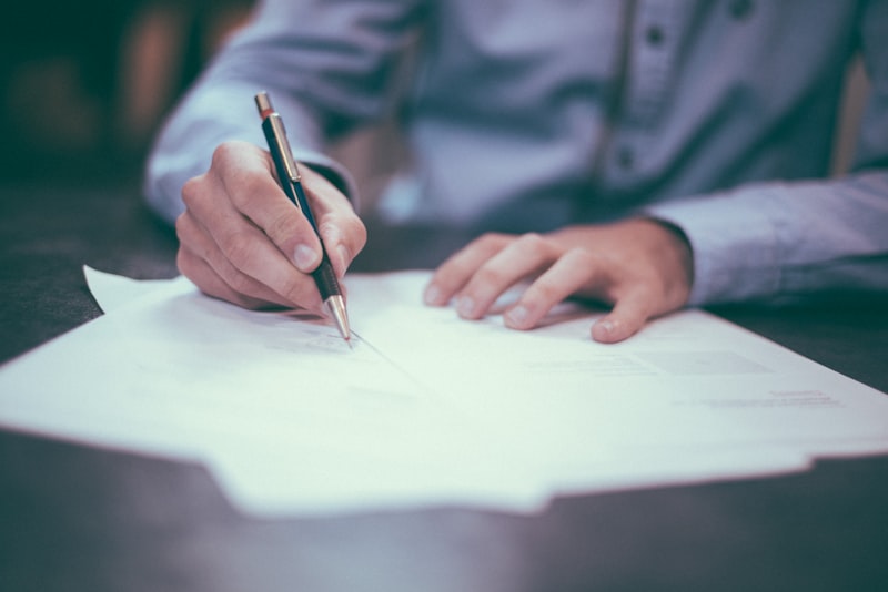 A person sitting at a wooden desk with papers and a calculator under soft light