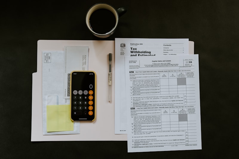 A wooden desk with a notebook, calculator and a cup of coffee beside a laptop