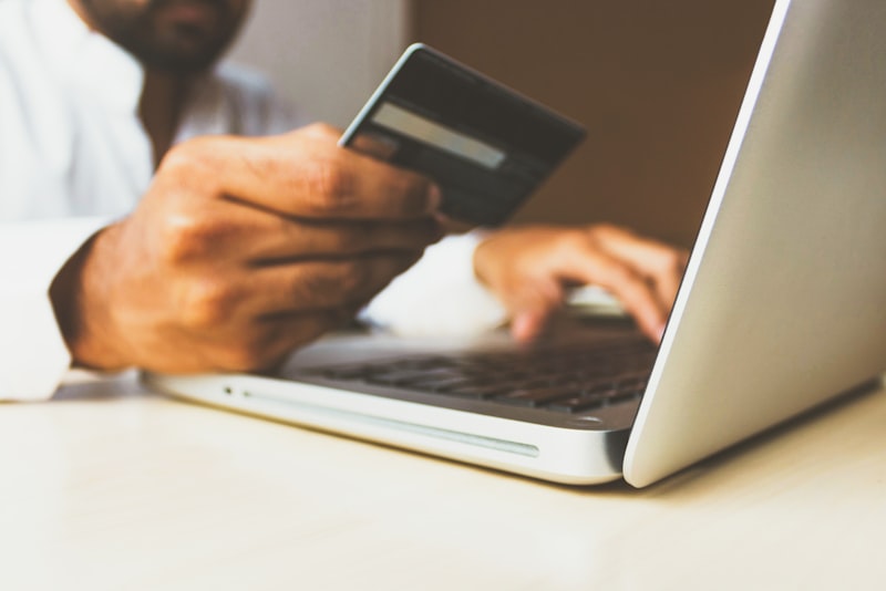 A person holding a bank card while looking at a laptop screen at a kitchen table